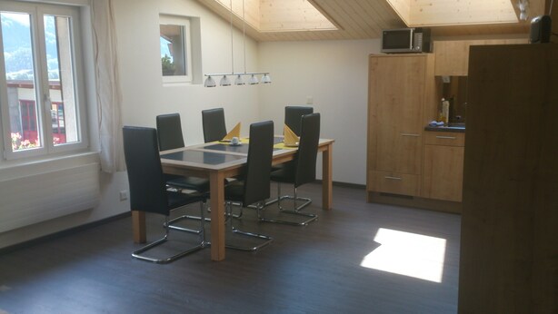 A dining area with a table and chairs, a small window, and a kitchen area with cabinets and a microwave.
