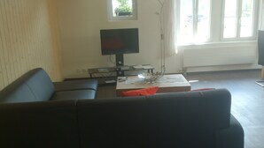 A living room with a black sofa, a coffee table with decorative items, a flat-screen TV on a stand, and a window with blinds.