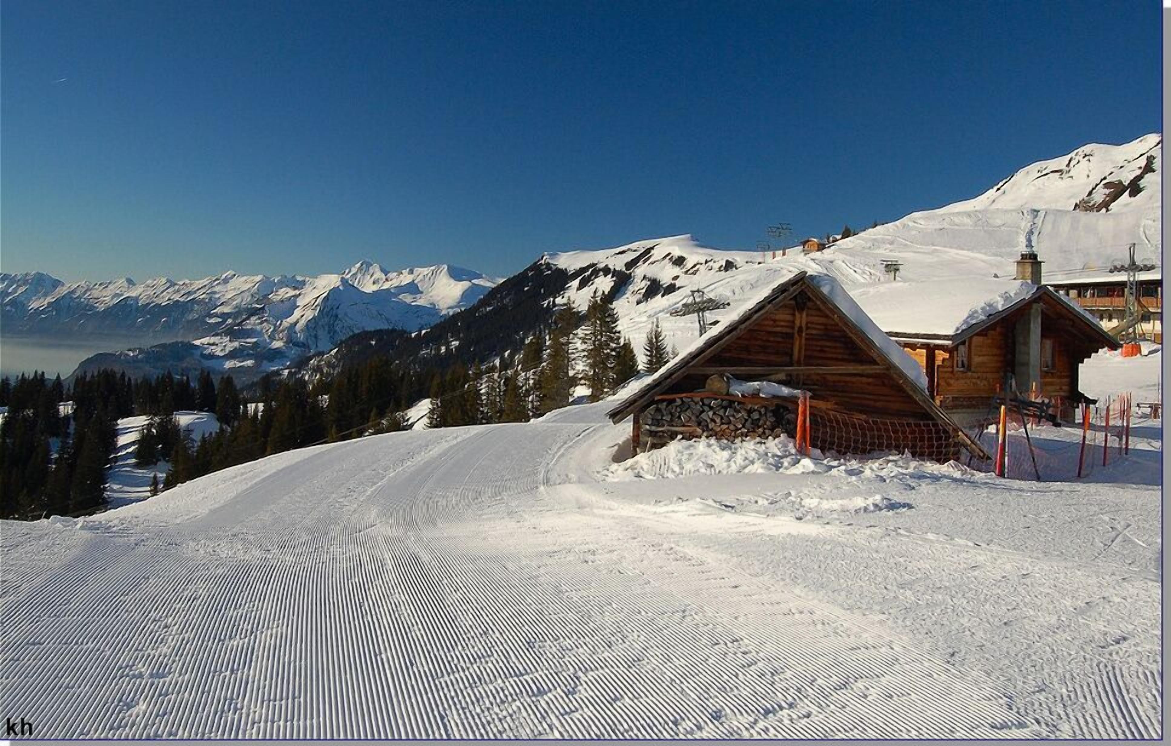 A snow-covered mountain with wooden cabins and ski tracks.