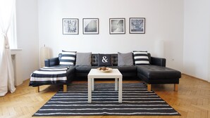 Un salon moderne avec un canapé d’angle en cuir noir, une table basse blanche et un tapis rayé noir et blanc. Quatre tableaux encadrés sont accrochés au mur au-dessus du canapé.