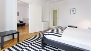 Une chambre à coucher moderne avec un grand lit, une petite table, un banc et une porte donnant sur une autre pièce.