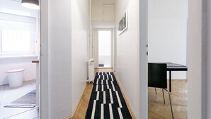 Un couloir avec un tapis à motifs noir et blanc, une chaise noire et un meuble blanc.