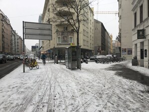 En snötäckt stadsgata med en busshållplats, cyklar och parkerade bilar.