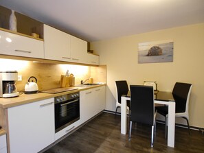 Una cucina compatta con mobili bianchi, forno integrato, bollitore e tavolo con sedie.
