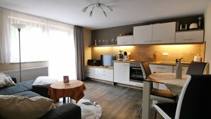 A modern kitchen with white cabinets, a dining table, and a sofa in a living area. - House Family Trube FeWo2 (Heringsdorf)