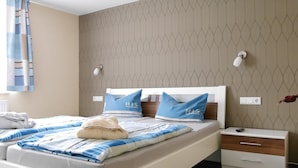 A neatly made bed with blue and white bedding, a bedside table with a lamp, and a wall with a geometric pattern. - House Family Trube FeWo2 (Heringsdorf)