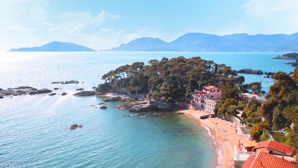 Una zona costiera con una spiaggia, una piccola isola con alberi e un edificio con tetto rosso.