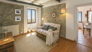 Una stanza accogliente con parete in pietra, pavimento in legno, un divano, una lampada e vista sull'esterno.