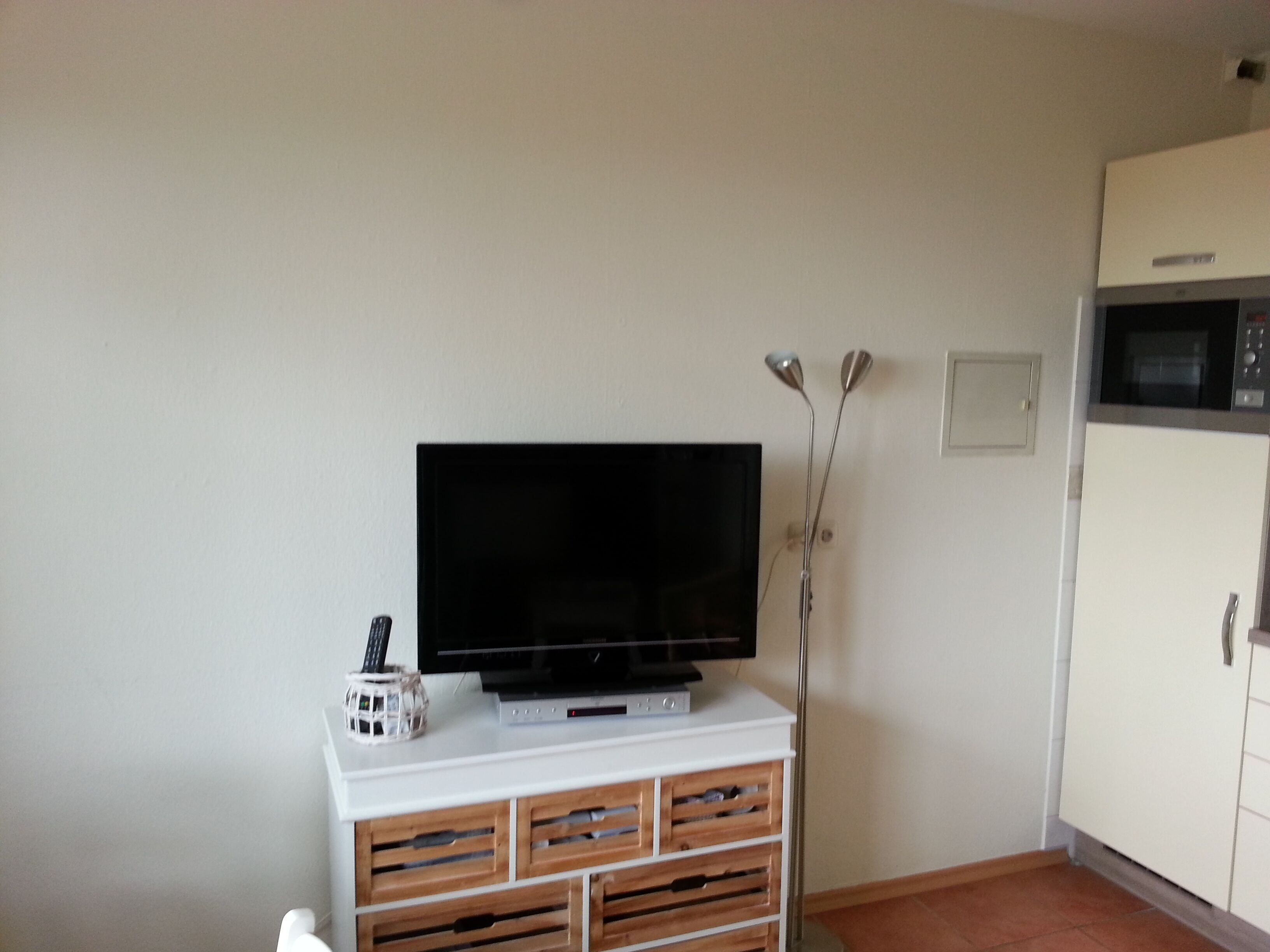 Une pièce avec un téléviseur à écran plat posé sur un meuble blanc, des tiroirs en bois en dessous, une porte blanche et un four à micro-ondes au-dessus.