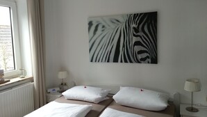 A hotel room with a bed, two bedside tables, a window with curtains, a wall-mounted zebra print artwork, and a radiator. - Experience the Baltic Sea up close and intense. (Haffkrug)
