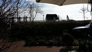 A patio area with a large umbrella, a rustic building, and a car parked nearby. - Experience the Baltic Sea up close and intense. (Haffkrug)