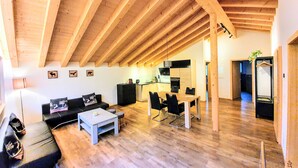 Un vaste espace de vie doté d’un haut plafond en bois, d’une table à manger avec des chaises, d’un canapé et d’une table basse.