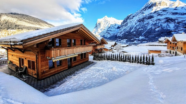 Un chalet en bois doté d’un balcon, entouré de montagnes enneigées et surplombant un ciel dégagé.