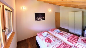 Une chambre avec un plafond en bois, un lit recouvert d’une couette à carreaux rouges et blancs, une image du ciel nocturne accrochée au mur et une armoire.