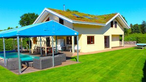 A house with a covered outdoor area, a swimming pool, and a well-maintained lawn.