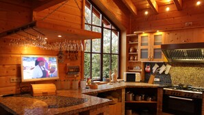 A rustic kitchen with wooden cabinets, a stone countertop, and a large window.