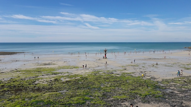 Una playa con un faro, orilla de arena y mar tranquilo.