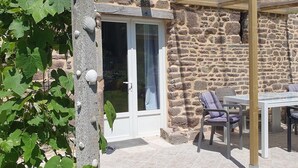 Un edificio de piedra con puerta de vidrio, asientos al aire libre y una pérgola.