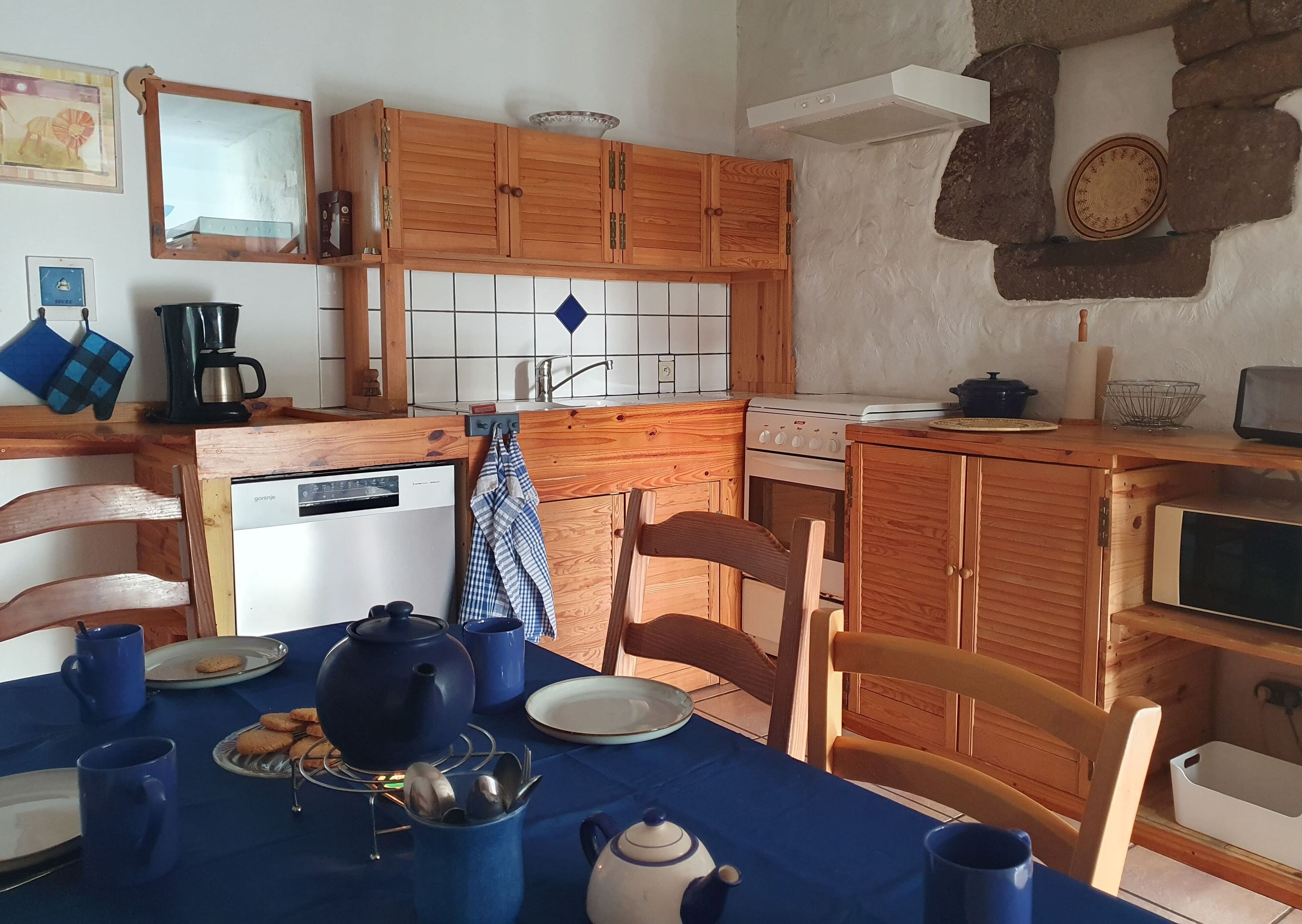 Una cocina acogedora con armarios de madera, una estufa y una mesa de comedor con vajilla azul.