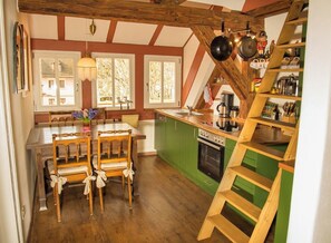Une cuisine avec des chaises en bois, une table à manger et un îlot central vert doté d’une plaque de cuisson.