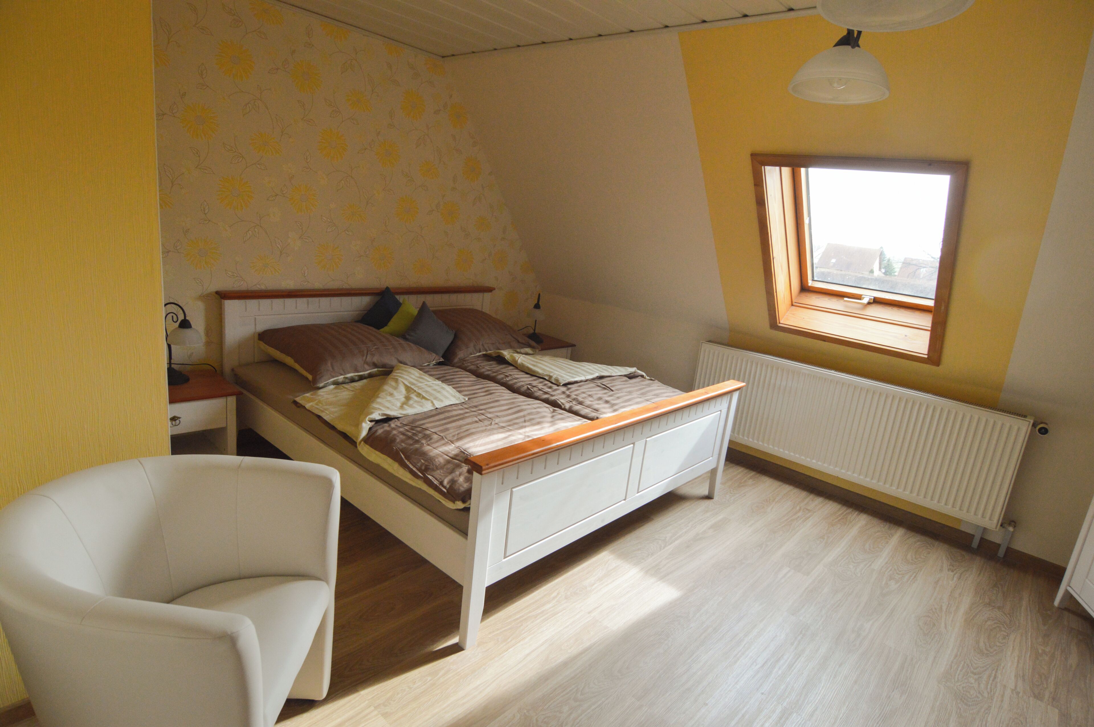Un dormitorio con cama, una silla, un ventanal y un radiador.