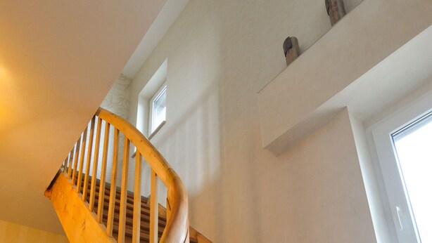 Eine Holztreppe mit geschwungener Geländer und einer Zwischenebene mit einem Fenster.
