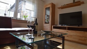 Ein modernes Wohnzimmer mit einem Glastisch, einem Ledersofa, einem Holzschrank und einem Flachbildfernseher.