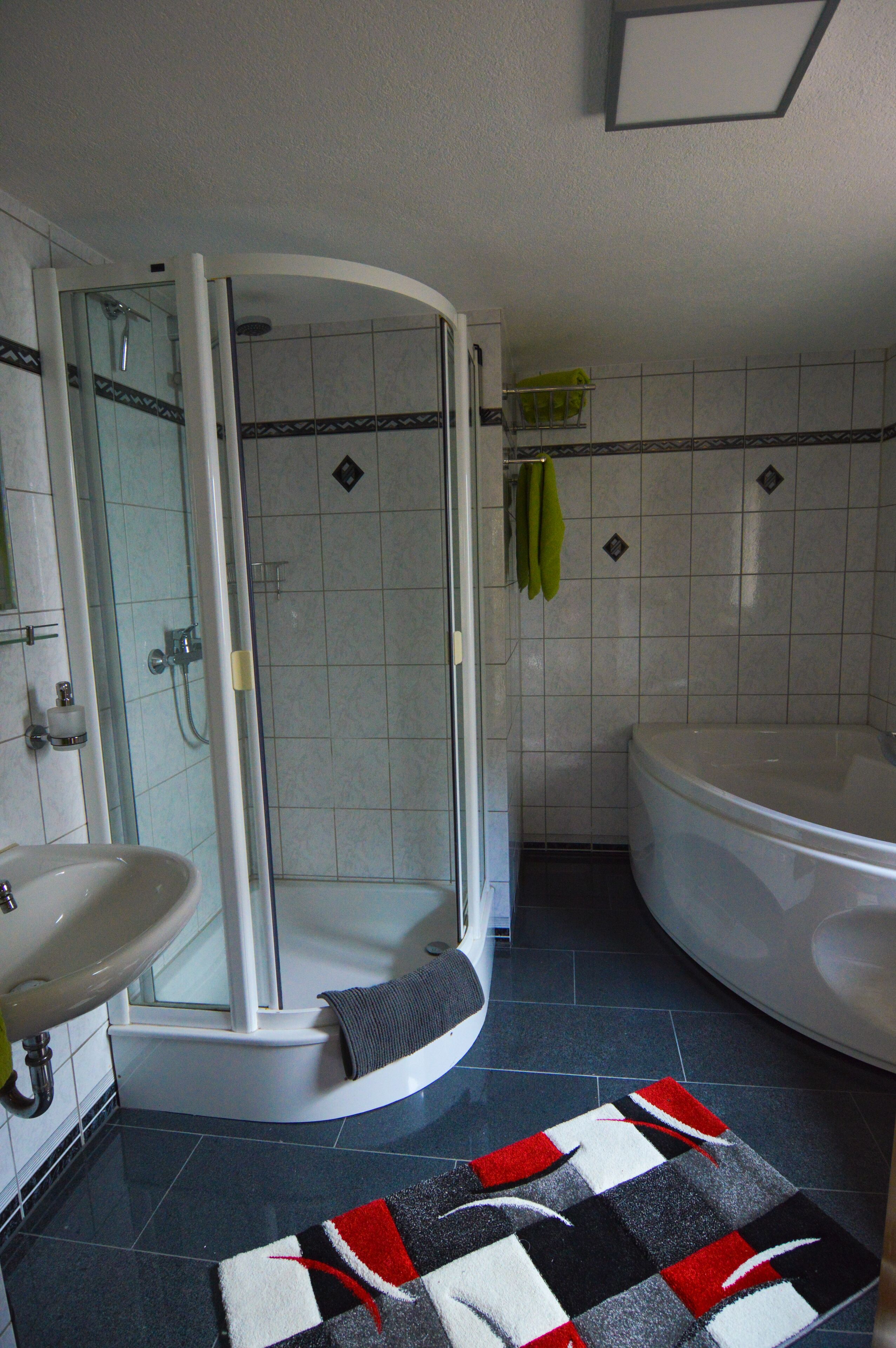 Een badkamer met een douche met glazen wand, een bad, een wastafel en een betegelde vloer.