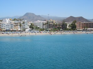 A coastal cityscape with a beach, buildings, and mountains in the background.