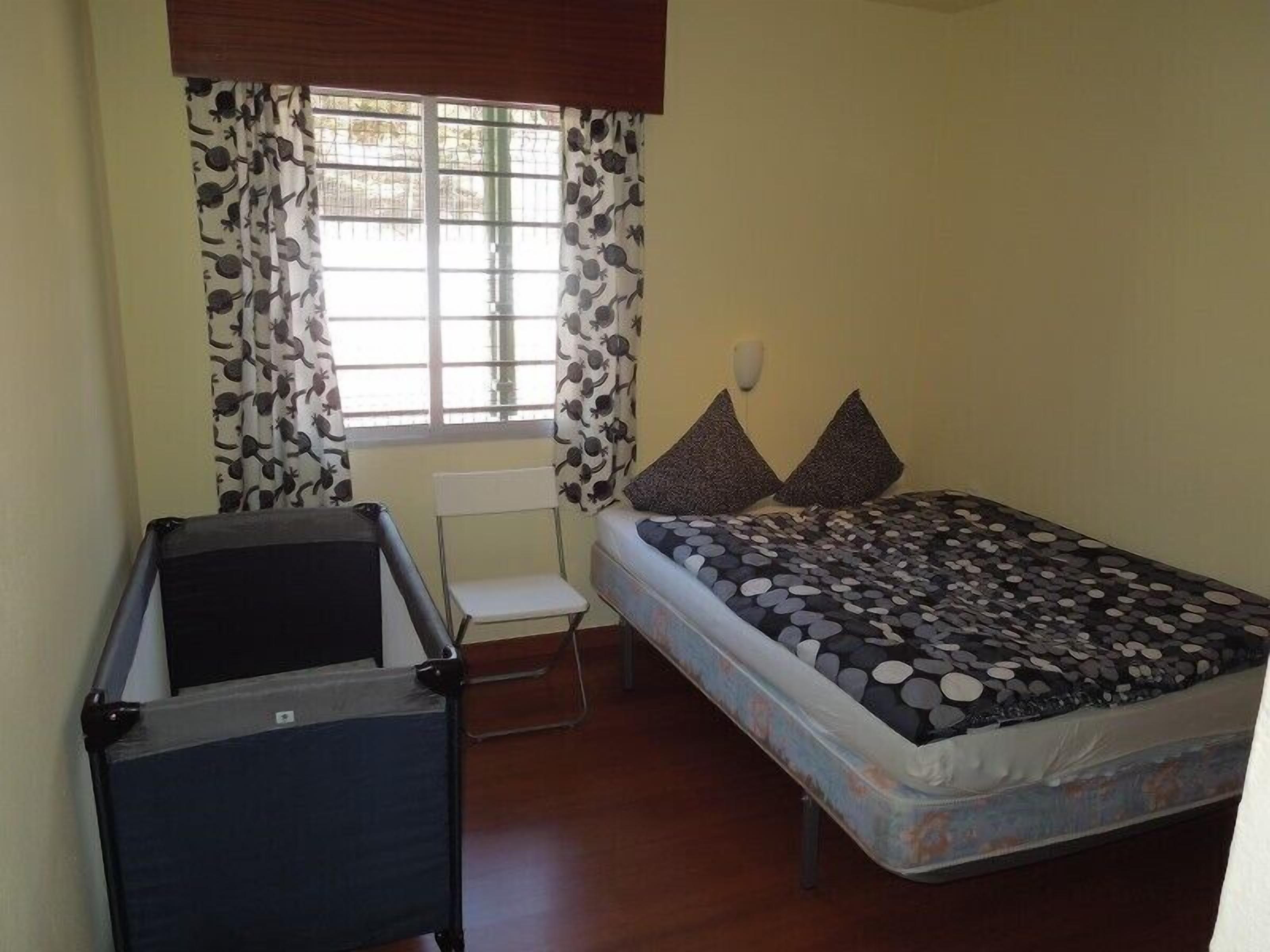 A bedroom with a bed, a chair, a small table, and a window with curtains.