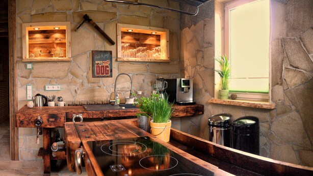 A kitchen with a stone wall, wooden counter, and a window with a plant. - Apartment "Chiara" (Oybin)