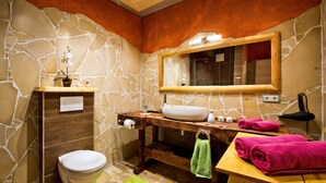 A bathroom with a stone wall, wooden vanity, a toilet, a sink, a mirror, and towels. - Apartment "Chiara" (Oybin)