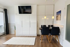 Una cocina moderna con televisor de pantalla plana, gabinetes blancos, una mesa de comedor con sillas y una alfombra blanca.