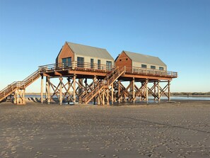 Un muelle de madera con un edificio sobre pilotes, que cuenta con varios niveles y una escalera.
