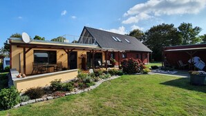 A two-story house with a patio, a satellite dish, and a garden. - Quiet situated bungalow with a terrace overlooking the water and in nature (Garz/Rügen)