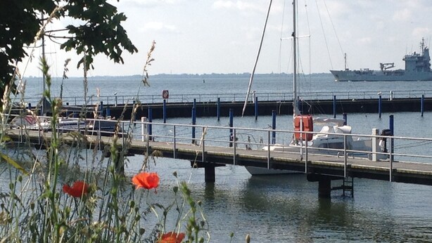 A dock with a ship in the background, a bridge, and a body of water. - Quiet situated bungalow with a terrace overlooking the water and in nature (Garz/Rügen)