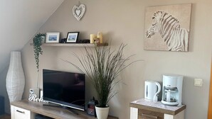 Ein Wohnzimmer mit Flachbildfernseher, Kaffeemaschine, Topfpflanze und einem Zebra-Kunstwerk an der Wand.