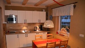 Kompakti keittiö, jossa on valkoiset kaapit, sisäänrakennettu mikroaaltouuni sekä ruokailutila, jossa on puinen pöytä ja tuolit.