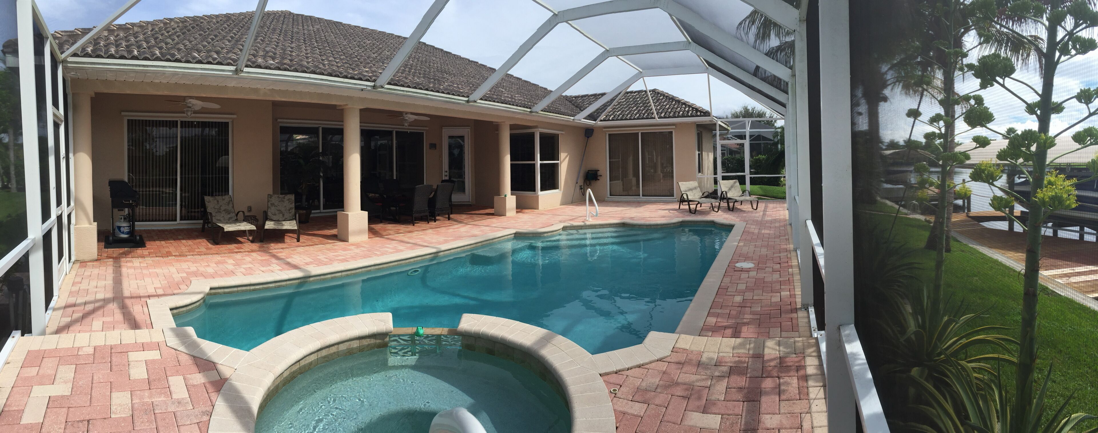 A swimming pool with a hot tub, patio furniture, and a covered area with chairs.