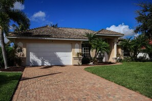 A two-story house with a white garage door, numbered 2218, surrounded by a well-maintained lawn and palm trees. - Dream villa in top location on the wide canal & large pool area with jacuzzi (Cape Coral)