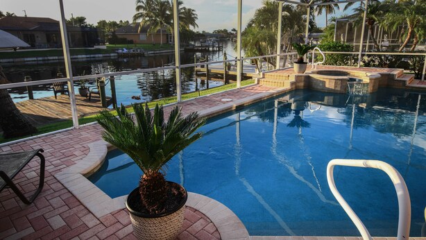 A pool with a clear view of the water, a palm tree, and a dock extending into the water. - Dream villa in top location on the wide canal & large pool area with jacuzzi (Cape Coral)