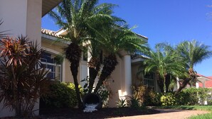 A paved pathway leading to a building with a tiled roof and palm trees. - Dream villa in top location on the wide canal & large pool area with jacuzzi (Cape Coral)
