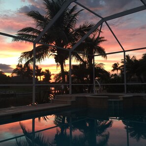 A pool area with a sunset view, surrounded by palm trees and a metal structure. - Dream villa in top location on the wide canal & large pool area with jacuzzi (Cape Coral)