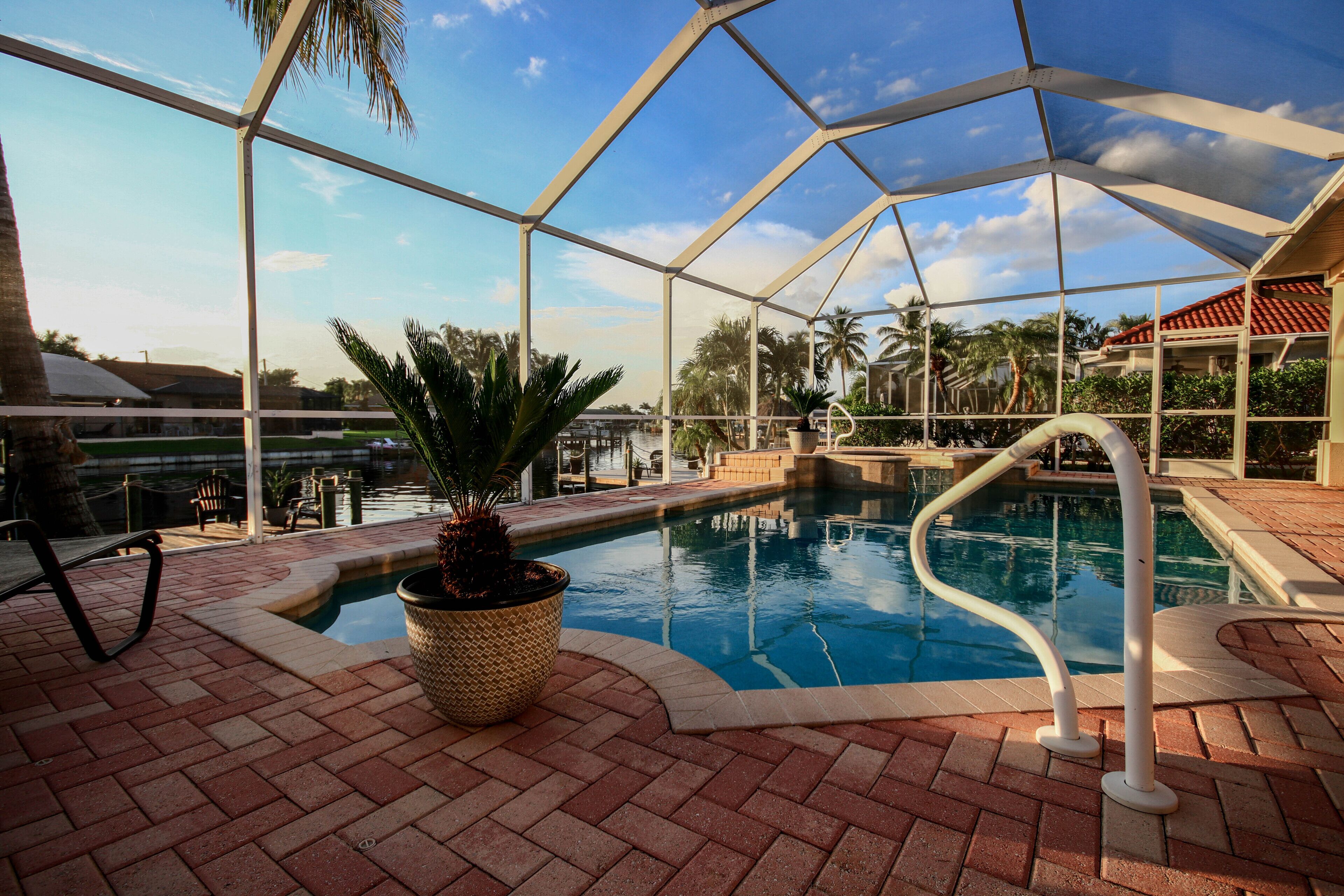An indoor swimming pool with a clear view of the surrounding area, including a palm tree and a building with a red roof.