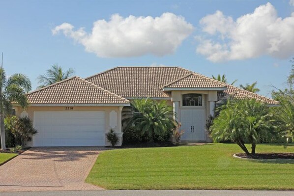 A single-story house with a tiled roof, a garage, and a well-maintained lawn with palm trees. - Dream villa in top location on the wide canal & large pool area with jacuzzi (Cape Coral)