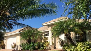 A two-story house with a garage, surrounded by well-maintained lawns and various plants. - Dream villa in top location on the wide canal & large pool area with jacuzzi (Cape Coral)