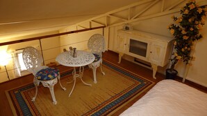 Een kamer met een bed, een klein rond tafeltje met stoelen, een kast en een plant in een pot.