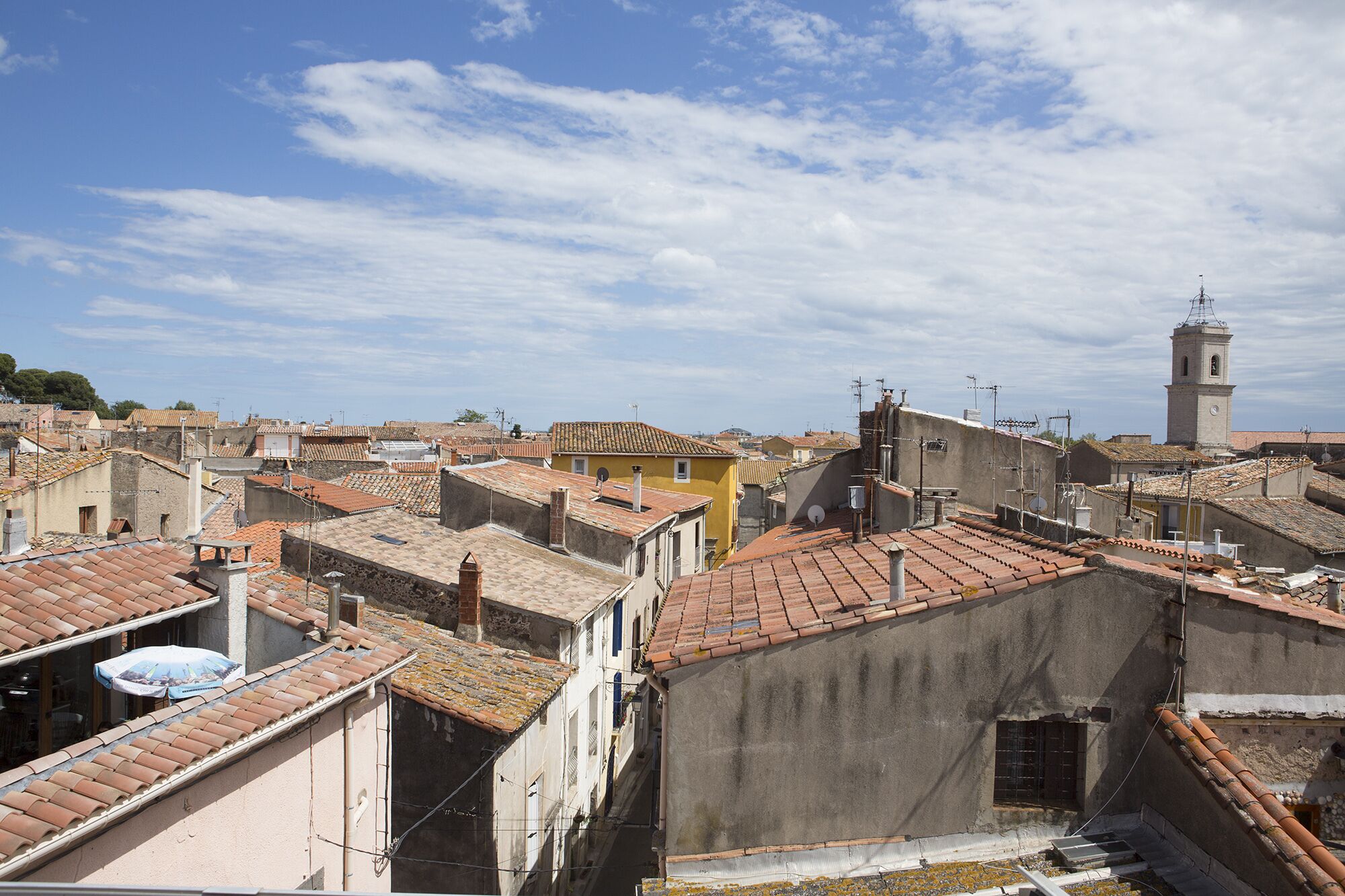Une zone urbaine densément peuplée, caractérisée par des toits traditionnels recouverts de tuiles en terre cuite, un clocher d’église imposant et une rue étroite.