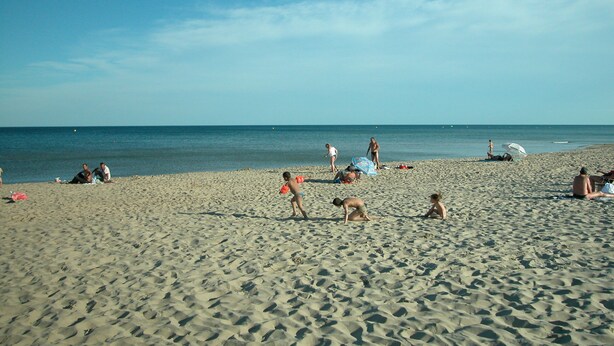 Een zandstrand met mensen die zonnebaden en spelen.