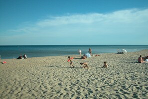 A sandy beach with people sunbathing and playing, a clear sky, and calm sea.